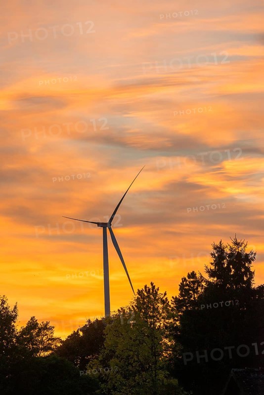 Stationary wind turbine, wind turbine, rotor blades and generator, silhouette, atmospheric sky in the evening, orange clouds at sunset, energy, power generation, electricity, lull, calm, trees, Lüneburg district, Lower Saxony, GermanySilhouette of a wind turbine in front of an orange sunset sky
