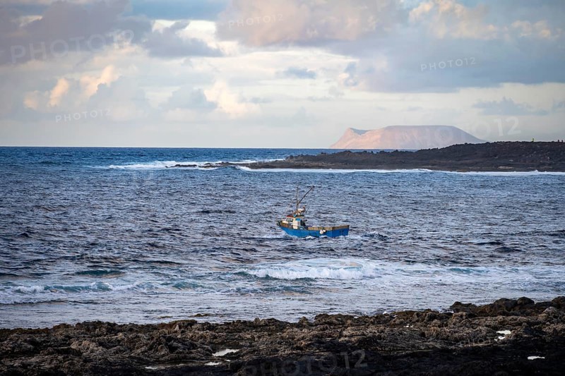 Fishing boat out to sea in the evening, seaside coast with volcanic rocks at sunset, La Santa, Lanzarote, Canary Islands, Spain