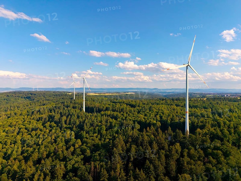 Three wind turbines stand in a green forest landscape under a clear sky, near Schorndorf, Rems-Murr-Kreis, Baden-Württemberg, Germany