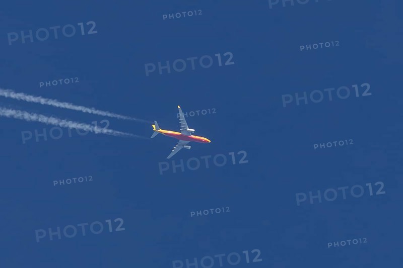 Boeing 767 jet cargo aircraft of DHL airlines flying in a blue sky with contrails or vapours trails behind, England, United Kingdom