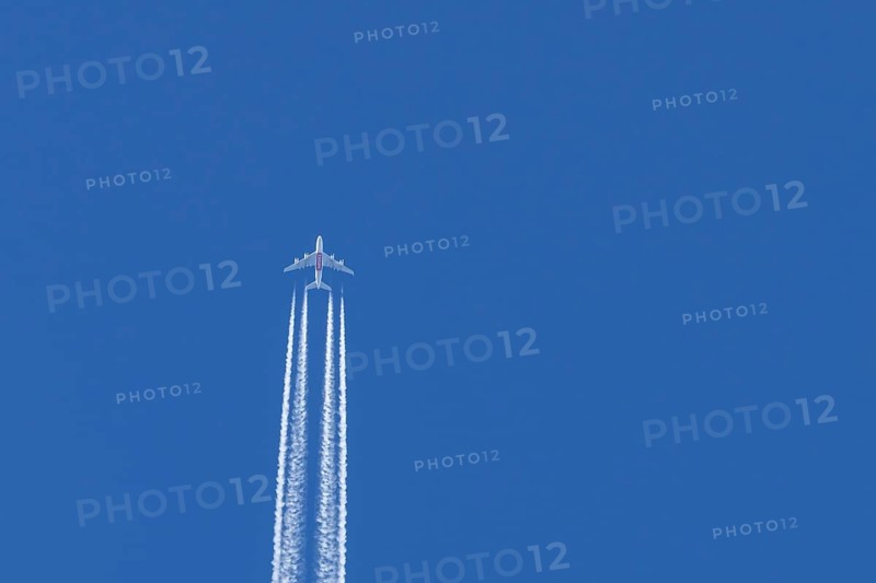 Airbus A380 jet passenger aircraft of Emirates airlines flying in a blue sky with contrails or vapour trails behind, England, United Kingdom