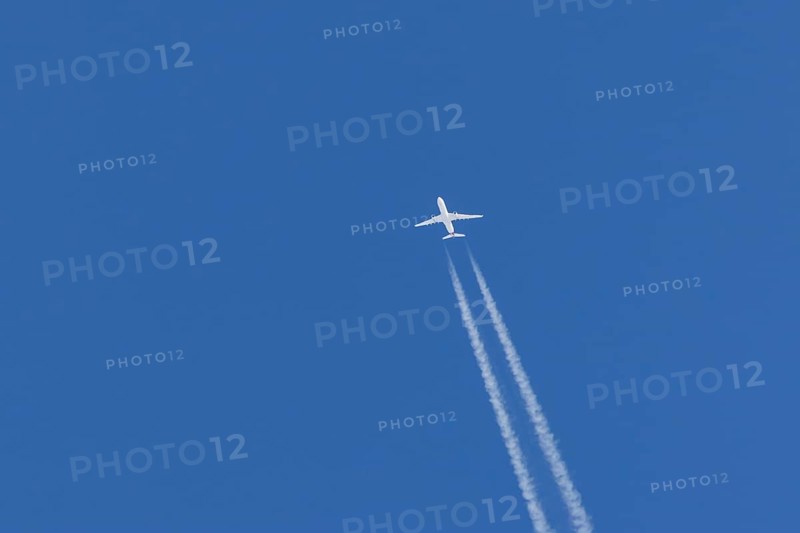 Jet passenger aircraft flying in a blue sky with contrails or vapour trails behind, England, United Kingdom