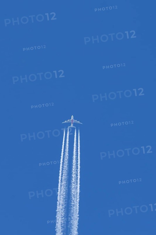Airbus A380 jet passenger aircraft of Emirates airlines flying in a blue sky with contrails or vapour trails behind, England, United Kingdom