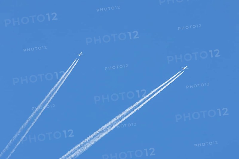 Two jet passenger aircraft flying in a blue sky with contrails or vapour trails behind, England, United Kingdom