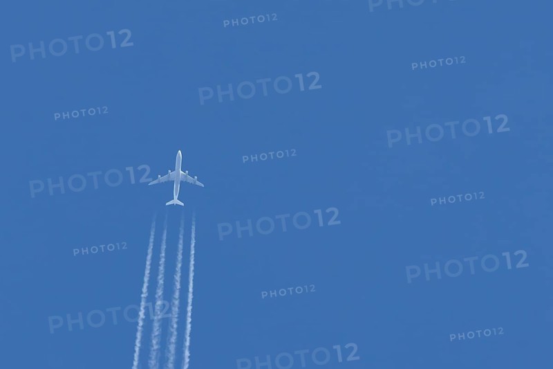 Jet passenger airliner aircraft flying in a blue sky with contrails or vapour trails behind, England, United Kingdom