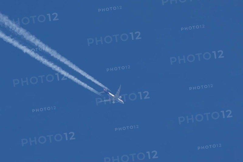 Boeing 777 jet cargo aircraft of FedEx Express airlines flying in a blue sky with contrails or vapour trails behind, England, United Kingdom