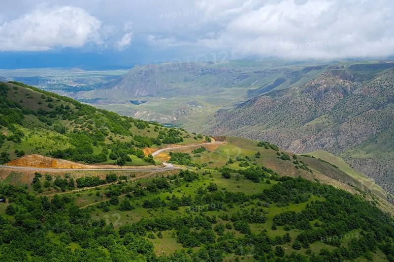 Wide green landscape with hills and a winding road under cloudy sky, landscape near Ltsen, Syunik province, Syunik, Caucasus, Armenia