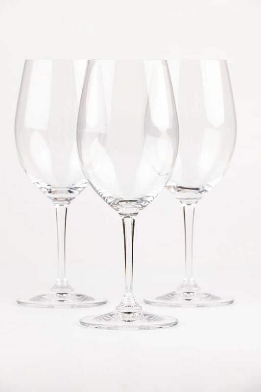 Three elegant, transparent wine glasses with long stems against a neutral background