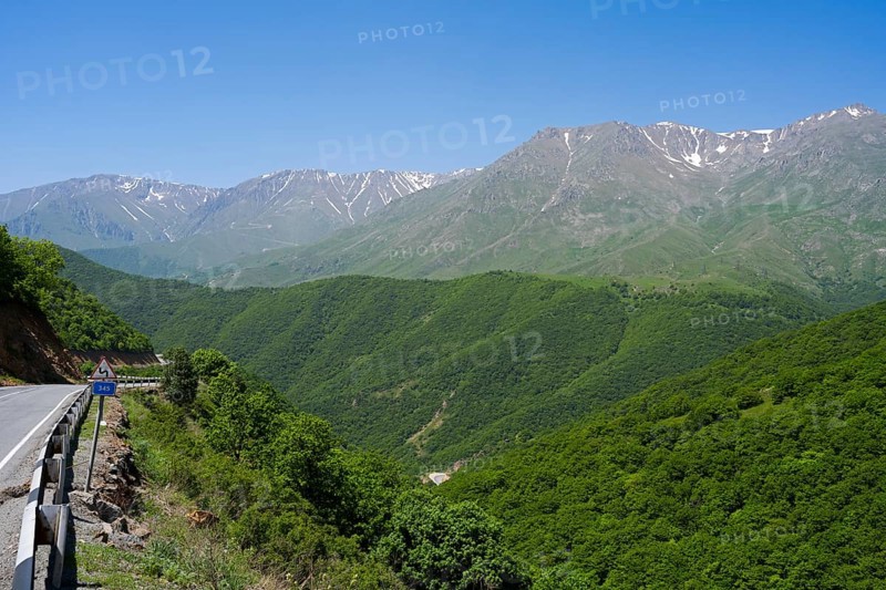 A winding mountain road snakes through green hills with mountains in the background, landscape on M2 near Meghri Pass, Tashtun Pass, Syunik Province, Armenia