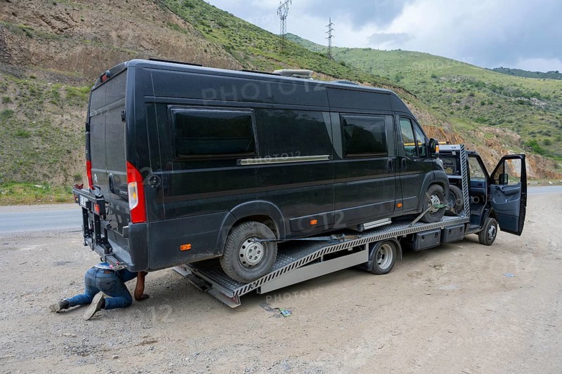 Black van on a car transporter, driver working under the vehicle, camper being towed, motorhome, Lernadzor, Syunik province, Caucasus, Armenia