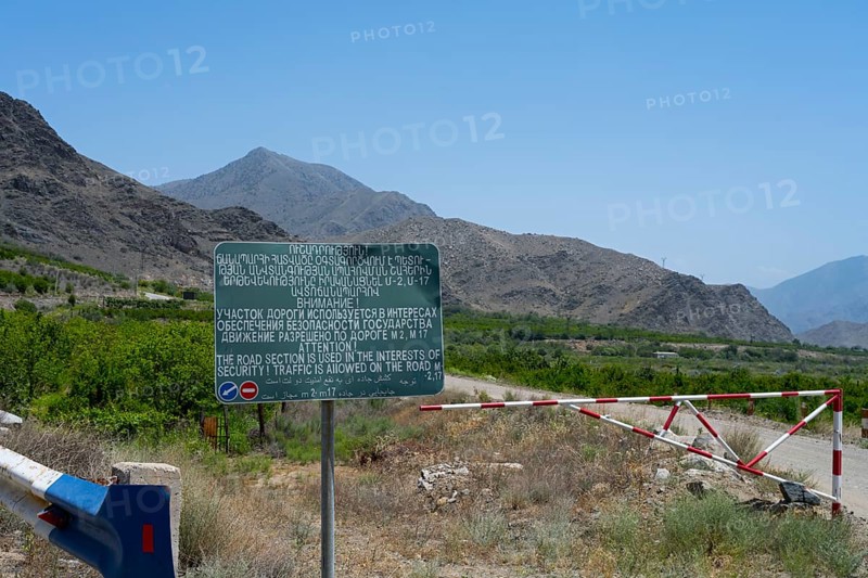 A sign and a barrier are on a road with safety warnings, sign on the M17 road that runs along the border with Azerbaijan, Syunik province, Armenia, AsiaA sign and a barrier stand on a mountain road with safety warnings