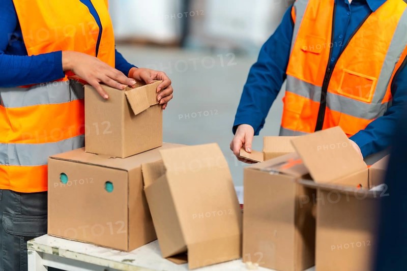 Warehouse workers in safety vests pack and sort cardboard boxes for shipment, demonstrating efficient logistics, team order fulfillment and industrial e commerce operations