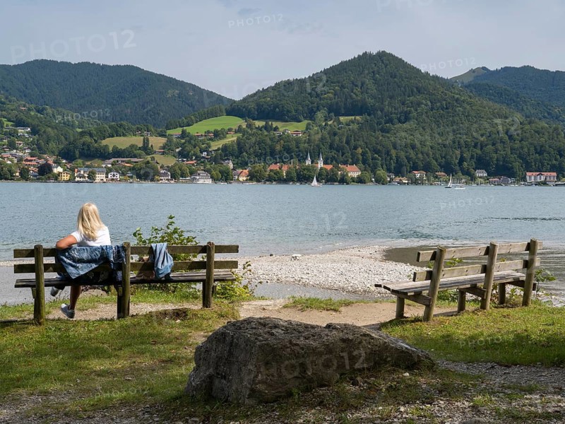 View of Tegernsee with castle, woman sitting on a bench, Bad Wiessee, Upper Bavaria, Bavaria, Germany