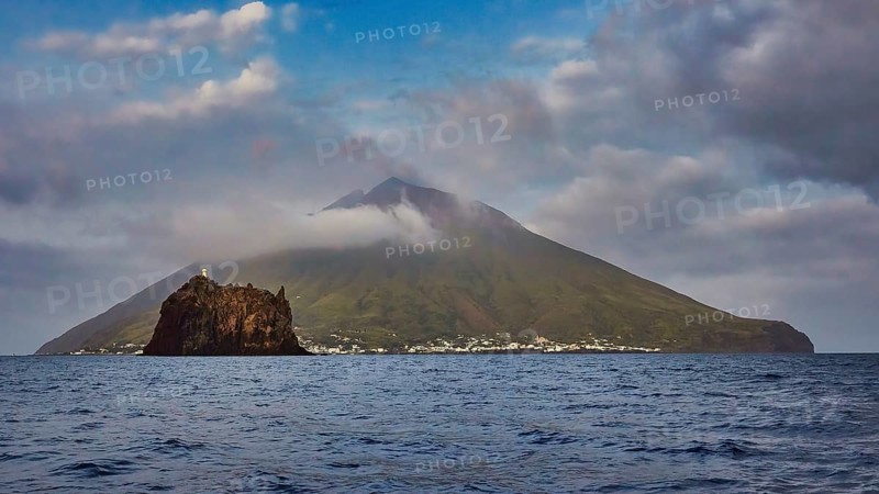 Stromboli island with offshore islet Strombolicchio, volcanic island with picturesque village surrounded by thick clouds and calm sea, UNESCO World Heritage Site, Aeolian Islands, Aeolian Islands, Sicily, Italy