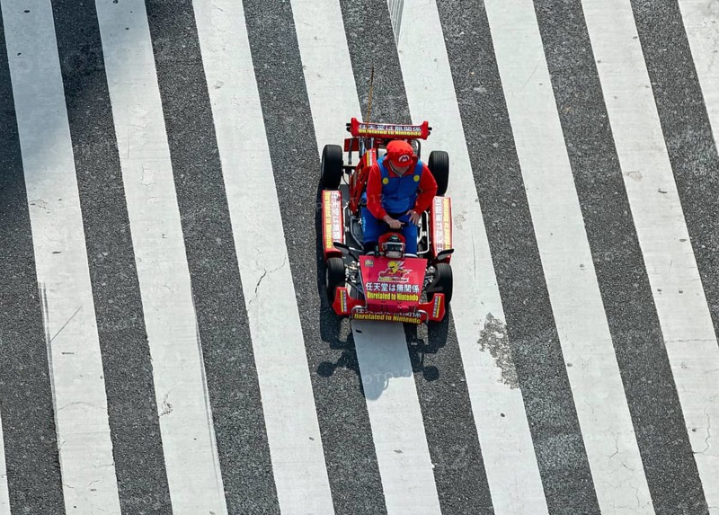 People in costumes drive small go-kart racing cars across zebra crossings, Shibuya Crossing, Shibuya, Tokyo