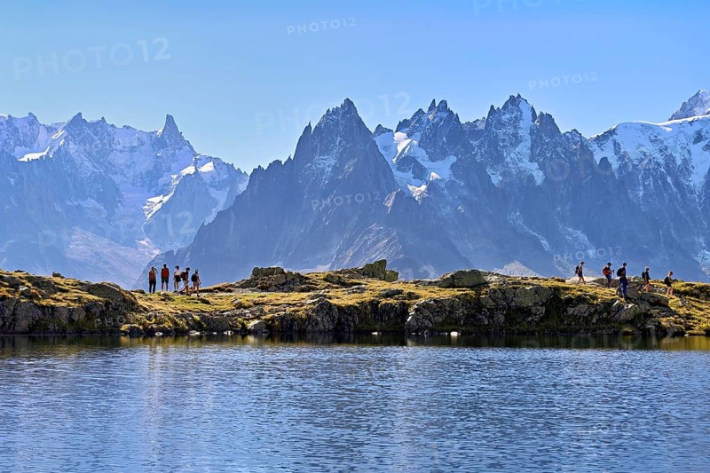 A group of hikers at Lac de Chésserys, behind the snow-covered Mont Blanc massif, Chamonix-Mont-Blanc, Haute-Savoie, France