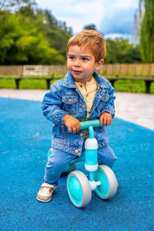 Cheerful toddler riding a balance bike in a vibrant playground, developing motor skills and enjoying outdoor fun, surrounded by colorful trees and a sunny atmosphere