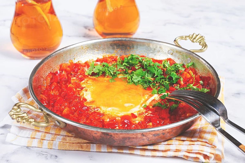 Traditional Turkish dish, scrambled eggs with tomatoes, Menemen, with herbs, in a frying pan, close-up, no people