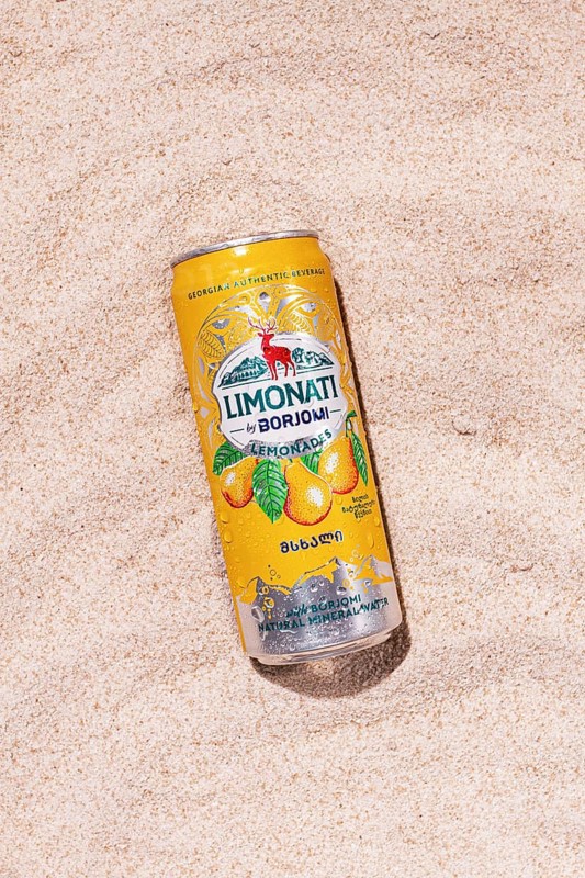 Carbonated lemonade with pear flavor, in an iron jar, Georgian drink, Borjomi, on a sandy beach, sunlight