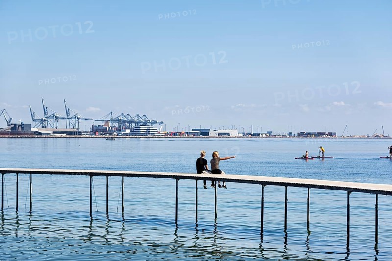 Two passers-by on circular bridge construction, wooden jetty, Infinite Bridge on Varna Beach, Ballehage Beach, architect Niels Povlsgaard, view of container port, Aarhus, Jutland, Denmark