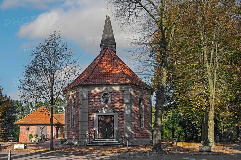 Brick chapel with pointed roof and roof turret, surrounded by autumn trees under a blue sky, Heek-Ahle, Münsterland, North Rhine-Westphalia, Germany