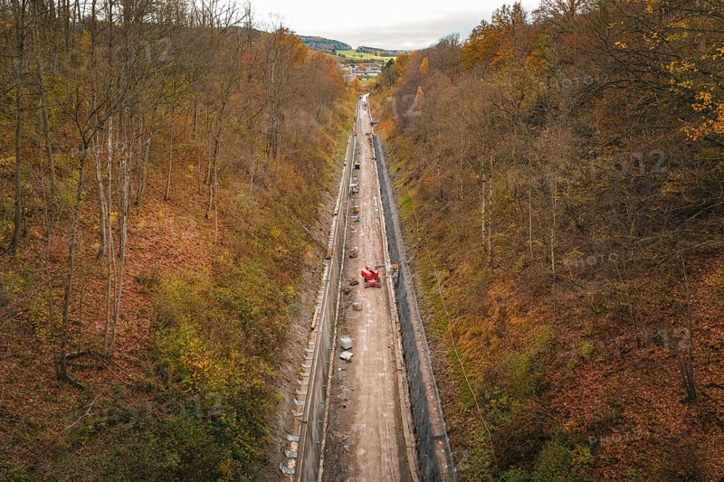 Aerial view of a construction site in an autumnal forest, with a long area of soil between steep slopes, construction of the Hermann Hesse Railway, Im Hau, Calw, Germany