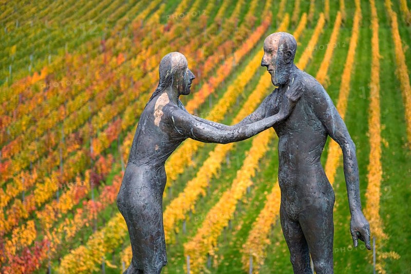 Two human figures as sculptures stand in front of colorful vines in an autumnal atmosphere, sculpture trail near Strümpfelbach im Remstal, Baden-Württemberg, Germany