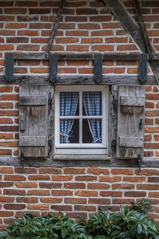 Rustic window with blue curtains and wooden shutters on the brick wall, Münsterland, North Rhine-Westphalia, Germany
