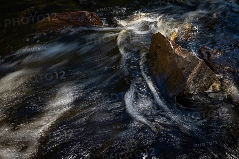 Current of a stream with dark water, reflections and turbulences, stones, long exposure, Sweden