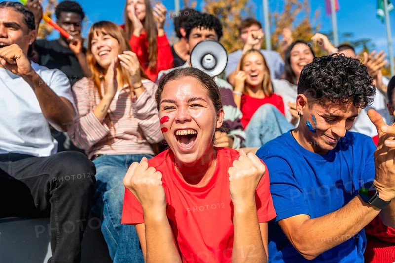 Young diverse fans sitting in a stadium enjoying a sporting event, celebrating and cheering for their team with excitement and passion, showing support and enthusiasm in a vibrant crowd