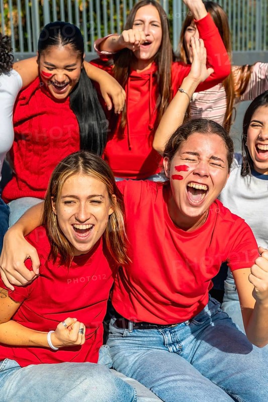 Diverse group of enthusiastic women celebrating and cheering for their favorite team at a sporting event, showing excitement, friendship, and strong fan support with red face paint
