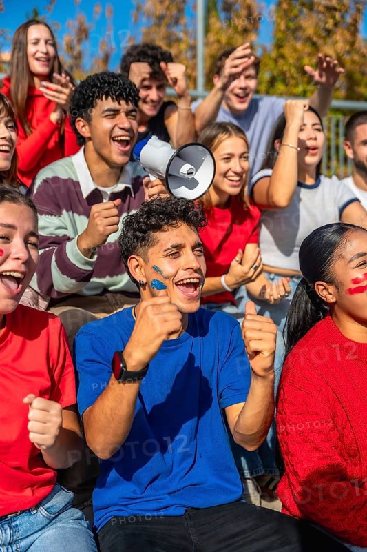 Young diverse fans intensely watching a sports game, cheering and celebrating together with face paint and a megaphone, showing team spirit and collective excitement in a stadium stands
