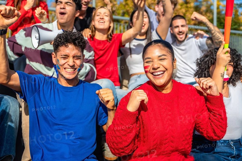 Diverse group of young sports fans cheering with painted faces and team colors in a stadium, celebrating together with joy, energy and unity during a daytime event