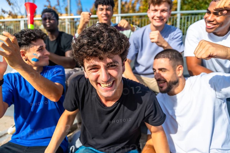Young diverse male friends cheering in a sunlit stadium, celebrating their team with smiles, laughter and high energy while bonding over sport and shared excitement