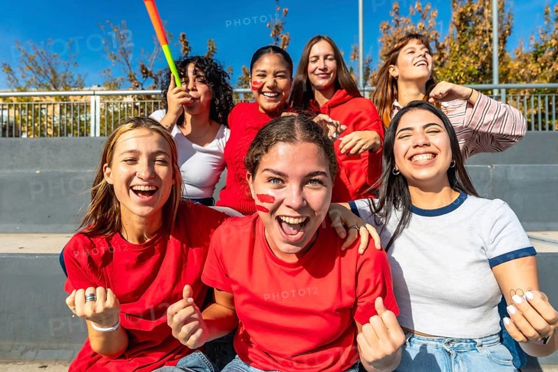 Group of excited young women in a stadium cheering, smiling and screaming for their team during a lively summer match, showing friendship, energy and winning spirit