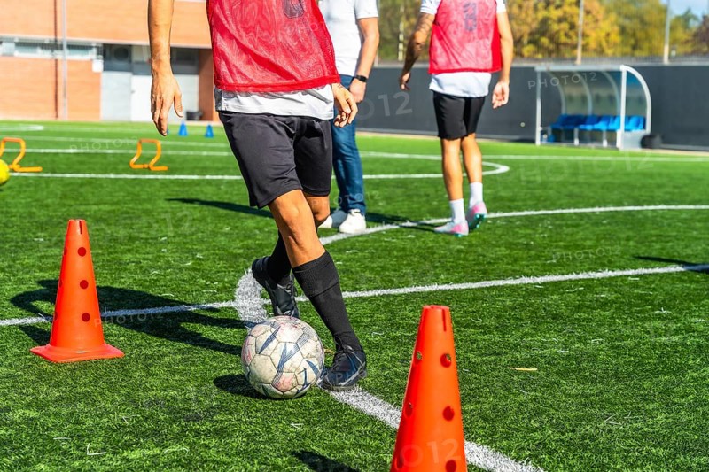 Football player practicing drills with ball and cones on artificial green turf, focused on improving skills, agility and control during outdoor training session