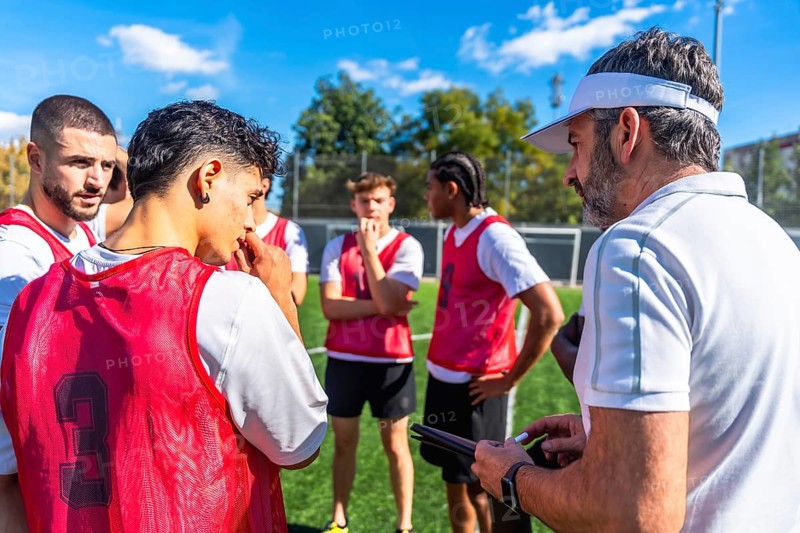 Soccer coach providing instructions and discussing game strategy with a group of young male team players listening attentively on the field during practice
