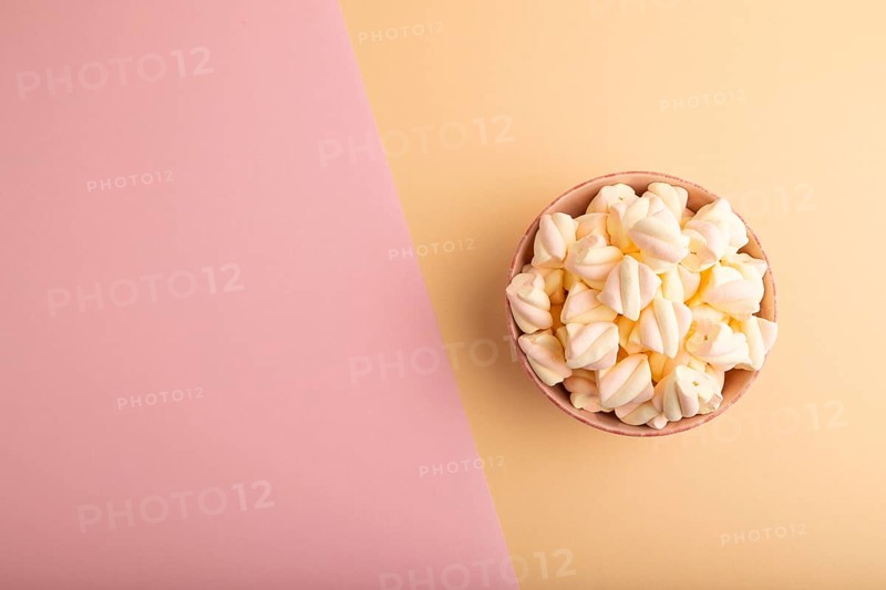 Orange and pink marshmallow in ceramic bowl on pink and orange pastel paper background, top view, flat lay, copy space, minimalism
