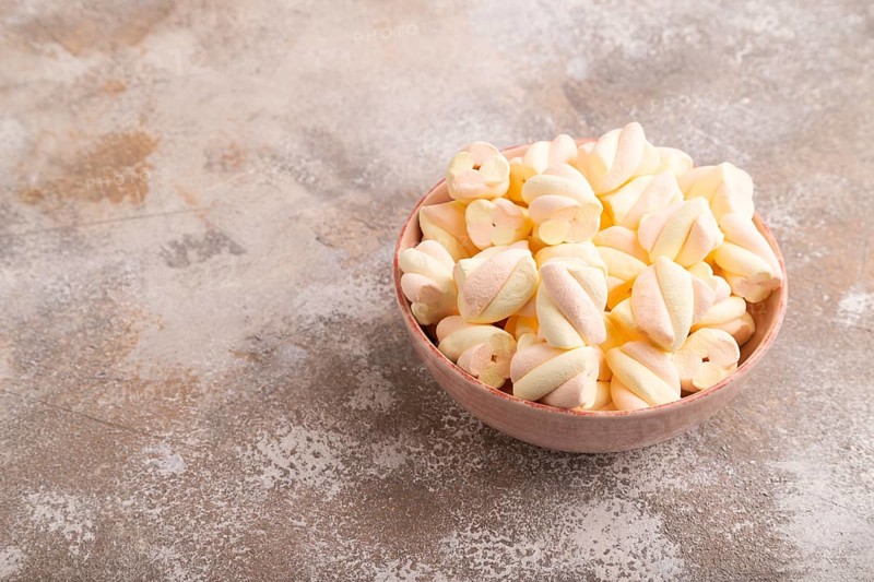 Orange and pink marshmallow in ceramic bowl on brown concrete background, side view, copy space, minimalism