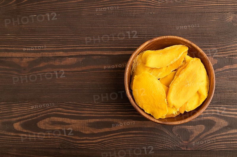 Dried Mango in wooden bowl on brown wooden background. Top view, copy space, flat lay. healthy food, minimalism