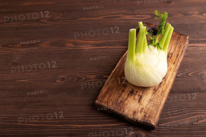 Fresh Fennel bulb on wooden cutting board on brown wooden background, side view, copy space, minimalism
