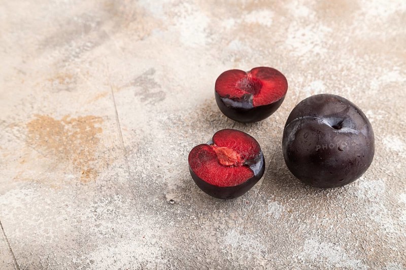 Purple Plum Cut in half on brown concrete background. Side view, copy space. healthy food, vegetable, minimalism