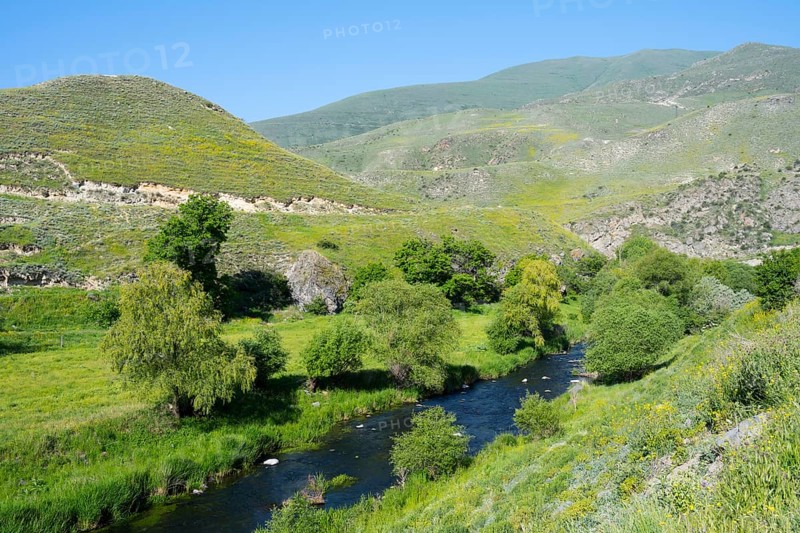 A green valley with a river and hills under a bright blue sky, picturesque nature, Vorotan River, Syunik Province, Armenia