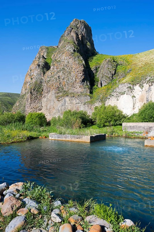 Clear water flows through a green landscape, framed by majestic, sunlit rocks, hot spring, Vorotan, Vorotan, Syunik province, Armenia