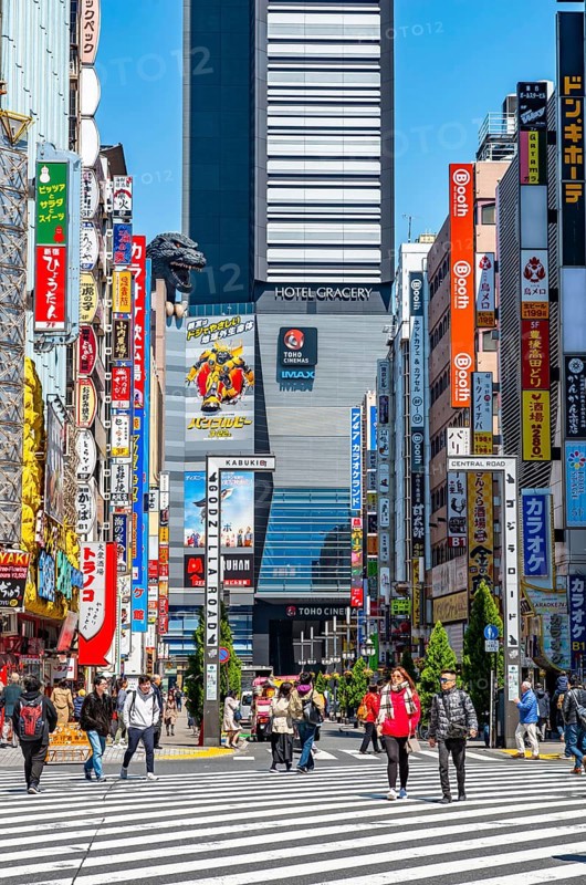 Bustling street scene in Japan with modern buildings and colorful billboards, figure of Godzilla head on a high-rise building, Shinjuku City, Tokyo, Japan