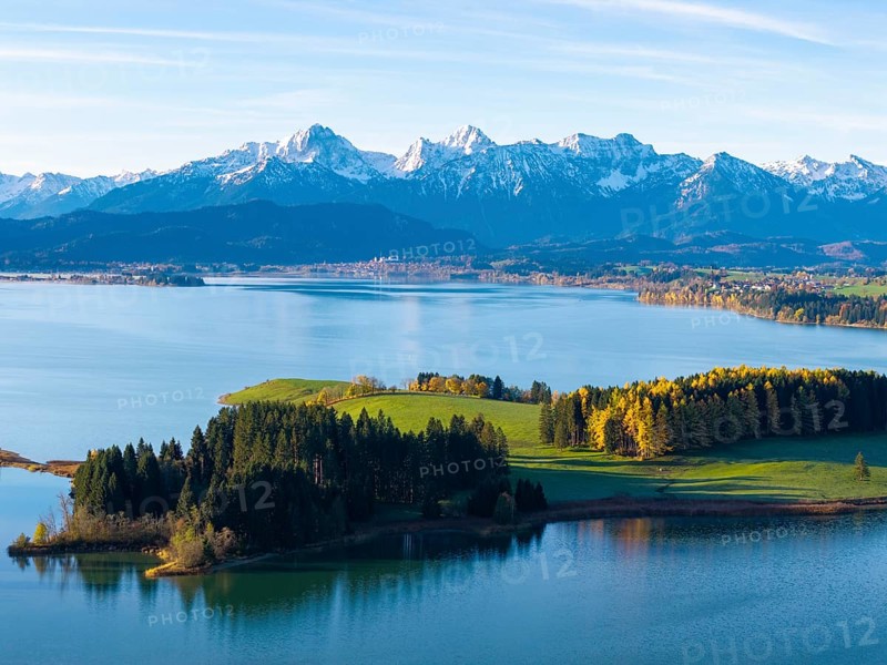 Idyllic mountain landscape with a calm lake, green hills and golden autumn trees under a blue sky