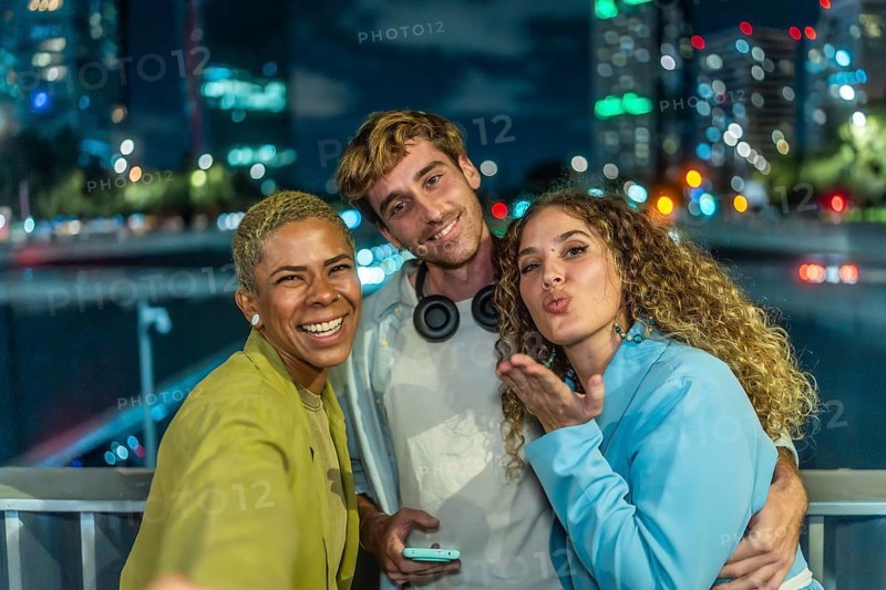 Diverse group of young adult friends enjoying a fun night out in the city, smiling and posing for a selfie against a backdrop of blurry urban lights, celebrating youth and modern friendship