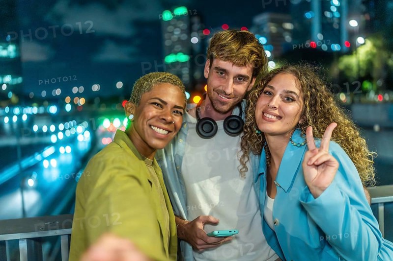 Group of diverse friends smiling and posing for a selfie at night, celebrating friendship and youth with city lights creating a vibrant urban background