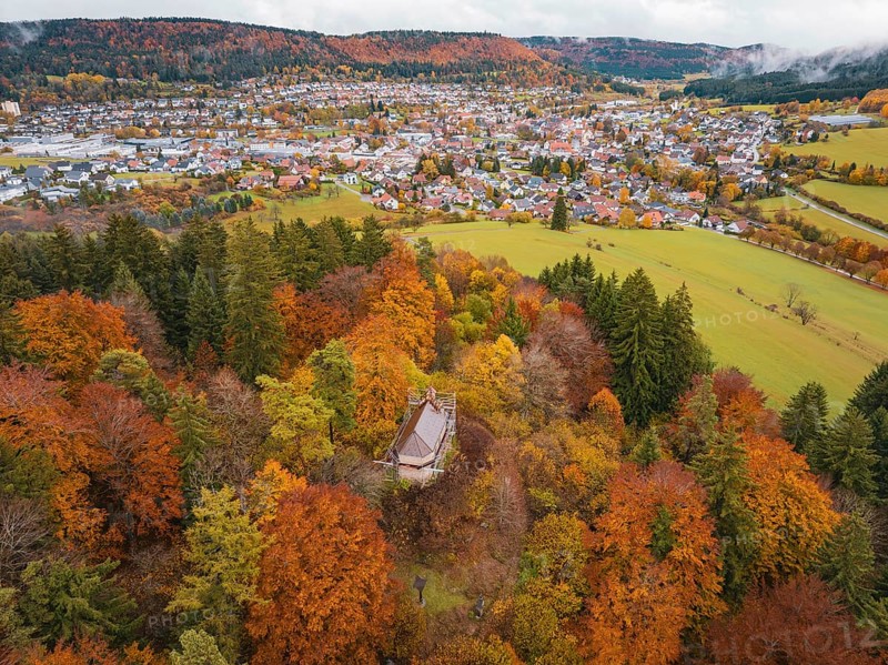 Pavilion in the middle of a colorful autumn forest with a view of a distant city and hills under cloudy sky, Wehingen, Tuttlingen district, Germany