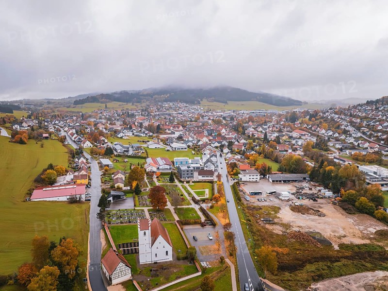 Aerial view of a village with church surrounded by fields, roads and wooded hills under a thick cloud cover, Wehingen, Tuttlingen district, Germany